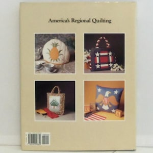 May include: A beige book titled America's Regional Quilting featuring four square photographs on the back cover. The images display a pineapple tea cozy, a red, white, and blue star-patterned tote bag, a tree-motif tote, and an eagle pillow.