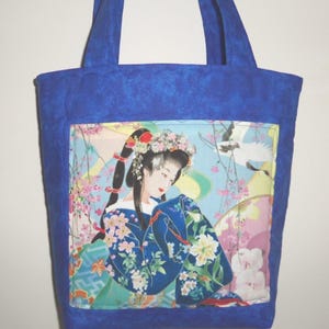 May include: A quilted blue tote bag featuring a central fabric panel with a printed illustration of a person in a floral kimono and hair ornaments, surrounded by cherry blossoms and a crane against a light blue background with two shoulder straps.