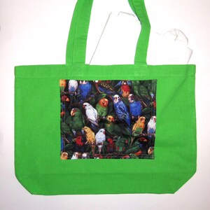 May include: A bright green tote bag featuring a rectangular central panel with a dense, colorful print of various parakeets and parrots perched among dark green foliage. The bag has two matching green fabric shoulder straps.