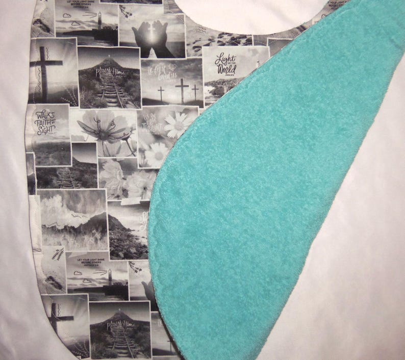 May include: A bib featuring a collage of black and white religious-themed images, including crosses, lighthouses, and flowers, with text such as Light of the World and Walk by Faith Not by Sight. The reverse side is a solid, textured turquoise fabric.
