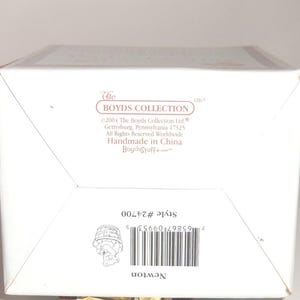 Op de afbeelding: Een witte doos met de tekst "The Boyds Collection" en "Newton". De doos bevat ook het stijlnummer #24700 en een barcode. Gemaakt in China.