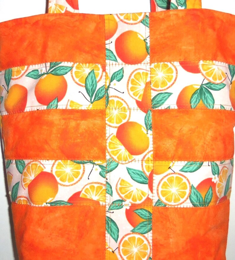 May include: Orange tote bag with a patchwork design. The bag features solid orange panels and patterned sections with orange fruit and green leaves on a white background. The bag has orange handles.