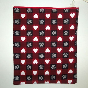 May include: Red and white checkered heating pad with a paw print and heart pattern. The heating pad is plugged in and ready to use.