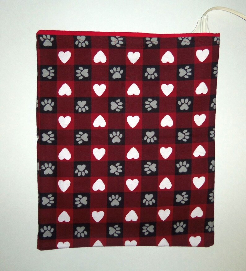 May include: Red and white checkered heating pad with a paw print and heart pattern. The heating pad is plugged in and ready to use.