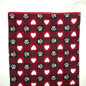 May include: Red and white checkered electric heating pad with a paw print and heart pattern. The pad is plugged in and ready to use.