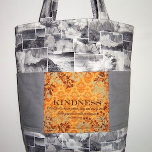 May include: A large tote bag with a patchwork design. The bag features a gray and white floral and landscape pattern, with a central orange panel that reads "KINDNESS" and a Bible verse. The bag has two handles.
