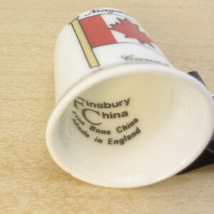 May include: White ceramic thimble with a red and white Canadian flag design. The bottom of the thimble reads "Finsbury China Fine Bone China Made in England."