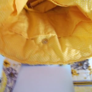 May include: A handmade yellow tote bag with a floral strap. The interior is a solid yellow, and the exterior features a yellow and white polka dot pattern. The strap has a floral design with yellow and purple flowers.
