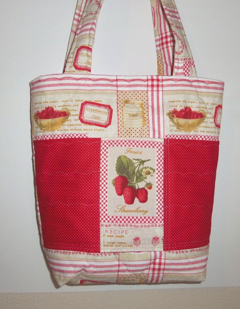 May include: A quilted tote bag featuring a patchwork design with red and beige stripes, polka dots, and strawberry-themed graphics. The centre panel displays a botanical illustration of strawberries with the text Fraise and Strawberry.