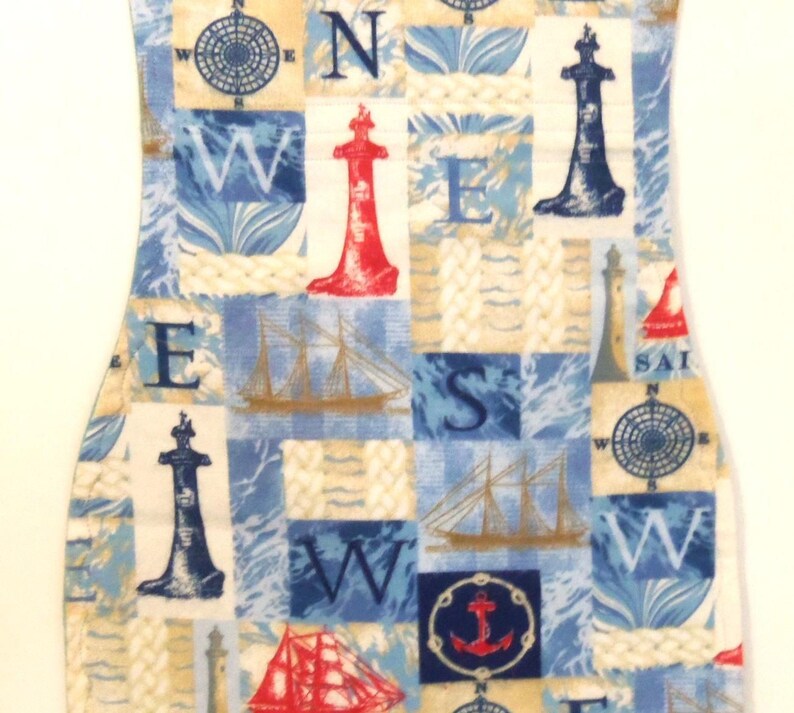 May include: A nautical-themed fabric with a repeating pattern of compasses, sailboats, anchors, and lighthouses in red, blue, and beige. The fabric is cut into a curved shape, possibly for a decorative item.
