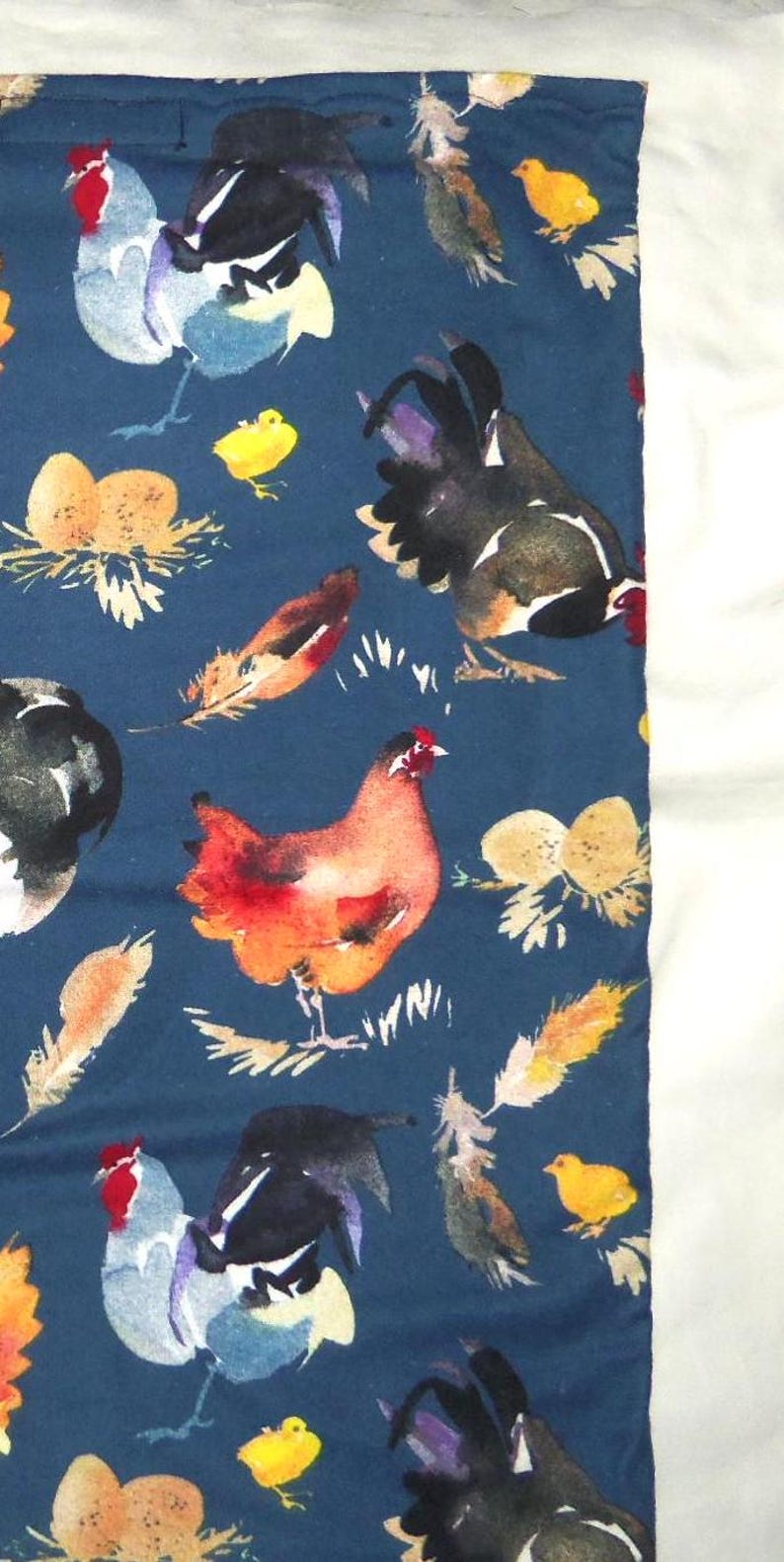 May include: A dark blue fabric featuring watercolor illustrations of chickens, roosters, chicks, feathers, and nests. The chickens are in shades of red, orange, black, and white. The chicks are yellow.