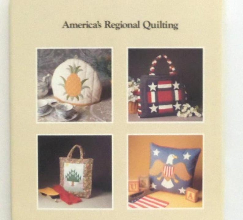 May include: A book titled America's Regional Quilting featuring four images: a pineapple-patterned tea cozy, a red, white, and blue star-patterned tote bag, a tree-patterned tote bag, and a blue pillow with a bald eagle and star design.