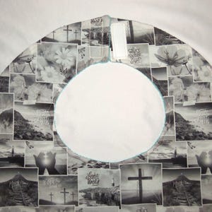 May include: A circular fabric tree skirt featuring a black and white collage print of religious imagery, including crosses, lighthouses, and hands, with the text "Walk by Faith not by Sight" and "Light of the World". It has a central opening and velcro.