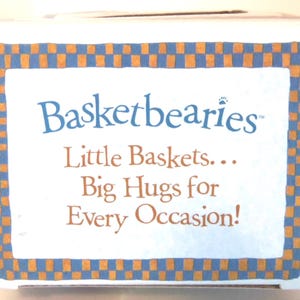 May include: A white box with the text "Basketbearies" in blue script, with the tagline "Little Baskets... Big Hugs for Every Occasion!" The box has a blue and orange checkered border.