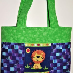 May include: A quilted tote bag featuring a bright green top section and handles. The lower portion displays a dark blue panel with a central graphic of a cartoon lion, surrounded by side panels with a purple and blue checkered pattern.