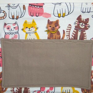 May include: White fabric with a brown pocket and a repeating pattern of colorful cartoon cats. The cats are wearing collars and some have bows.