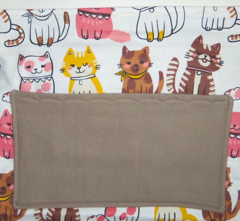 May include: White fabric with a brown pocket and a repeating pattern of colorful cartoon cats. The cats are wearing collars and some have bows.