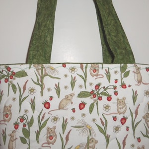 May include: A quilted tote bag featuring a white fabric base with a repeating pattern of small brown mice, red strawberries, and white flowers on green stems. The bag includes two sturdy olive green fabric handles at the top.