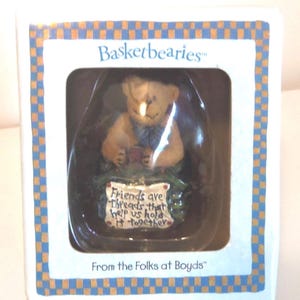 May include: A small, boxed figurine from Basketbearies. The figurine is a light brown bear holding a small red object. The box has a blue and orange checkered border and text that reads "Friends are threads that help us hold it together."