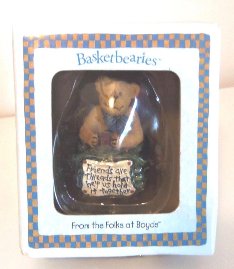 May include: A small, boxed figurine from Basketbearies. The figurine is a light brown bear holding a small red object. The box has a blue and orange checkered border and text that reads "Friends are threads that help us hold it together."