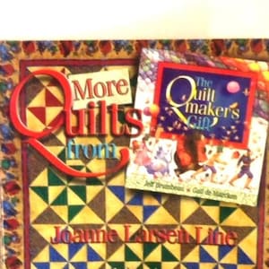 K&ouml;nnte beinhalten: Ein Buch mit dem Titel More Quilts von Joanne Larsen Line mit einem Steppmuster-Cover aus gelben, gr&uuml;nen und blauen Dreiecken. Ein kleineres Buch mit dem Titel The Quiltmaker's Gift liegt oben auf dem Cover.