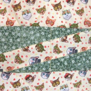K&ouml;nnte beinhalten: Ein gesteppter Stoffbezug mit einem sich wiederholenden Muster aus Katzen, die verschiedene Accessoires wie Brillen, H&uuml;te und Blumenkr&auml;nze tragen, auf cremefarbenem Hintergrund, durchzogen von zwei diagonalen B&auml;ndern aus dunkelgr&uuml;nem Stoff mit wei&szlig;em Blumenmuster.