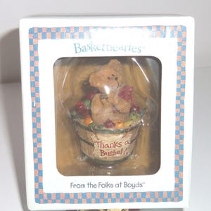 Op de afbeelding: Een doos met een "Basketbearies" beeldje. Het toont een kleine bruine beer met een rode strik, zittend in een houten mand gevuld met kleurrijk fruit. De mand heeft de tekst "Thanks a Bushel!". De doos heeft de tekst "From the Folks at Boyds".
