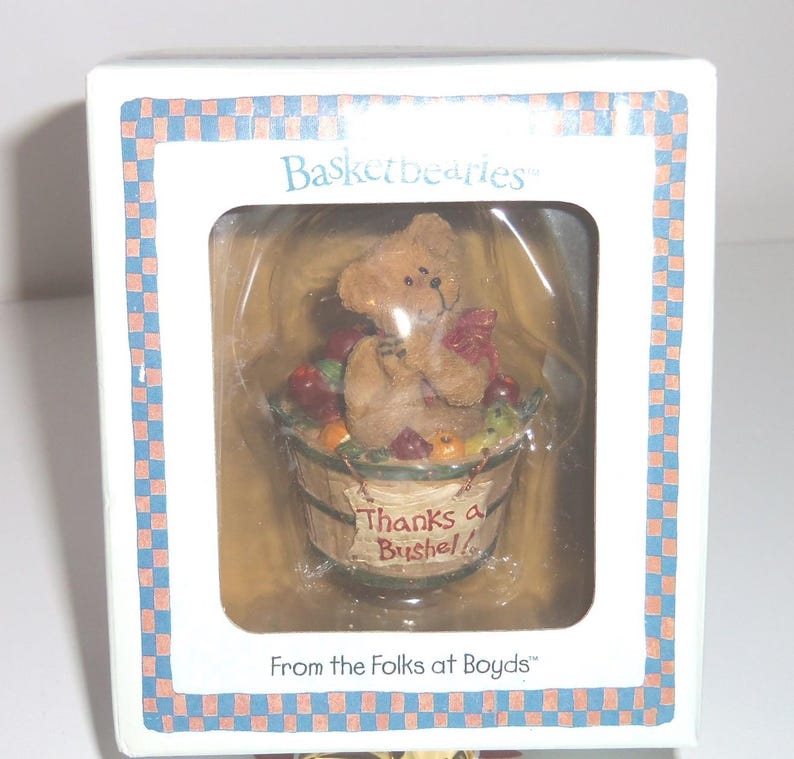 Op de afbeelding: Een doos met een "Basketbearies" beeldje. Het toont een kleine bruine beer met een rode strik, zittend in een houten mand gevuld met kleurrijk fruit. De mand heeft de tekst "Thanks a Bushel!". De doos heeft de tekst "From the Folks at Boyds".