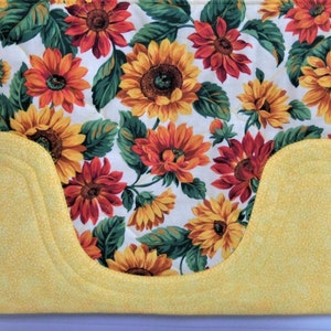 May include: A yellow quilted fabric tote bag with a sunflower print. The bag has a curved pocket on the front.