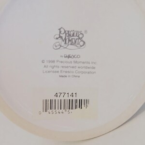 May include: A white ceramic mug base featuring the Precious Moments logo, the text 1998 Precious Moments Inc. All rights reserved worldwide Licensee Enesco Corporation Made in China, the number 477141, and a barcode with the number 0 45544 5.