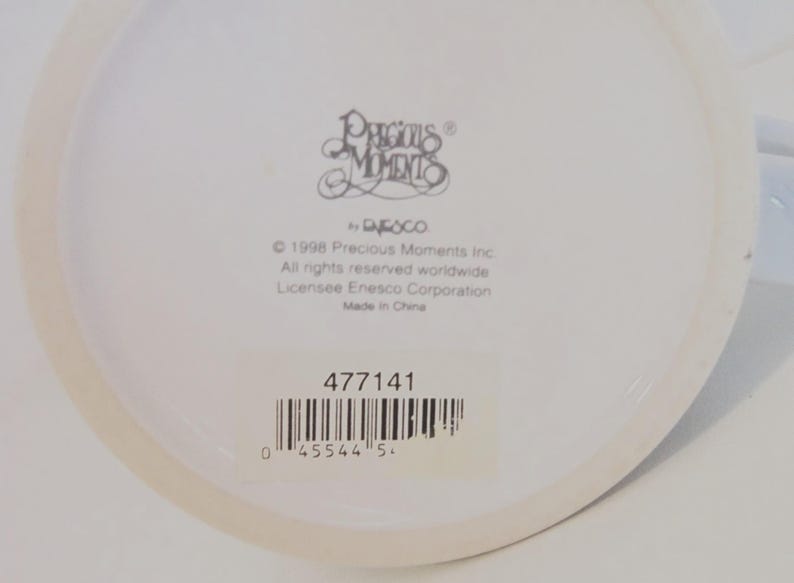 May include: A white ceramic mug base featuring the Precious Moments logo, the text 1998 Precious Moments Inc. All rights reserved worldwide Licensee Enesco Corporation Made in China, the number 477141, and a barcode with the number 0 45544 5.