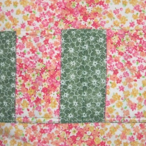May include: A fabric bag featuring a repeating floral pattern in shades of pink, orange, and yellow on a white background. The exterior includes a horizontal band of alternating vertical panels of green floral fabric and pink floral fabric.