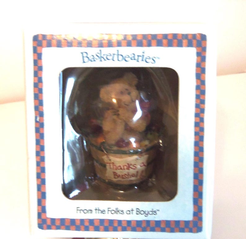 Op de afbeelding: Een beeldje in een doos van "Basketbearies" met een beer die een fruitmand vasthoudt. De beer is lichtbruin en de mand heeft de tekst "Thanks a Bushel". De doos heeft een blauw-oranje geruite rand.