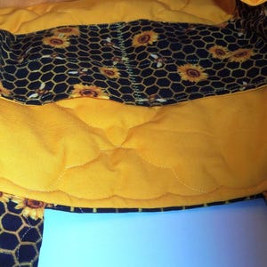 May include: A quilted fabric bag interior featuring a bright yellow lining and a black pocket panel decorated with a repeating pattern of yellow sunflowers and honeycombs. The bag has a soft, padded texture with visible stitching throughout.