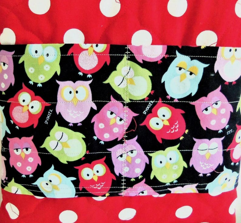 May include: A quilted fabric item featuring a red background with white polka dots and a central horizontal black band decorated with a repeating pattern of colourful owls in shades of pink, green, and blue, with the word snooz printed on some.