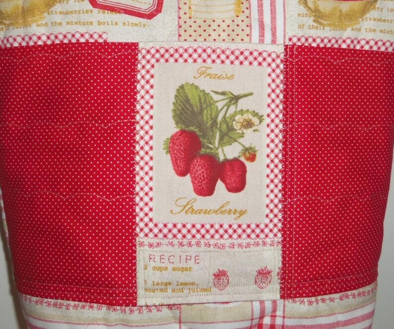 May include: A quilted fabric panel featuring a central rectangular patch with a botanical illustration of strawberries, the French word Fraise, and the English word Strawberry. The patch includes recipe text and red polka dot side panels.