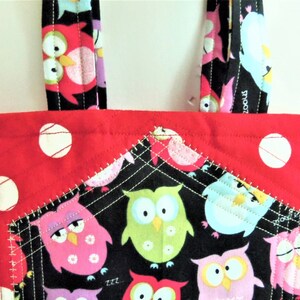 May include: A quilted tote bag featuring a vibrant red fabric with white polka dots and a black front pocket decorated with a colourful owl pattern. The bag includes matching black fabric handles with an owl print and white stitched details.