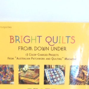 May include: A yellow craft book titled Bright Quilts From Down Under, featuring 13 color-charged projects from Australian Patchwork and Quilting magazine. The cover displays four small photographs of colorful, patterned quilts on a bright yellow background.