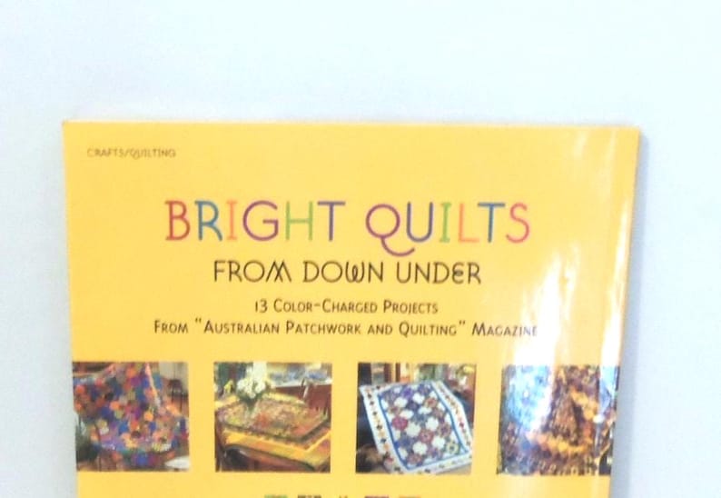 May include: A yellow craft book titled Bright Quilts From Down Under, featuring 13 color-charged projects from Australian Patchwork and Quilting magazine. The cover displays four small photographs of colorful, patterned quilts on a bright yellow background.