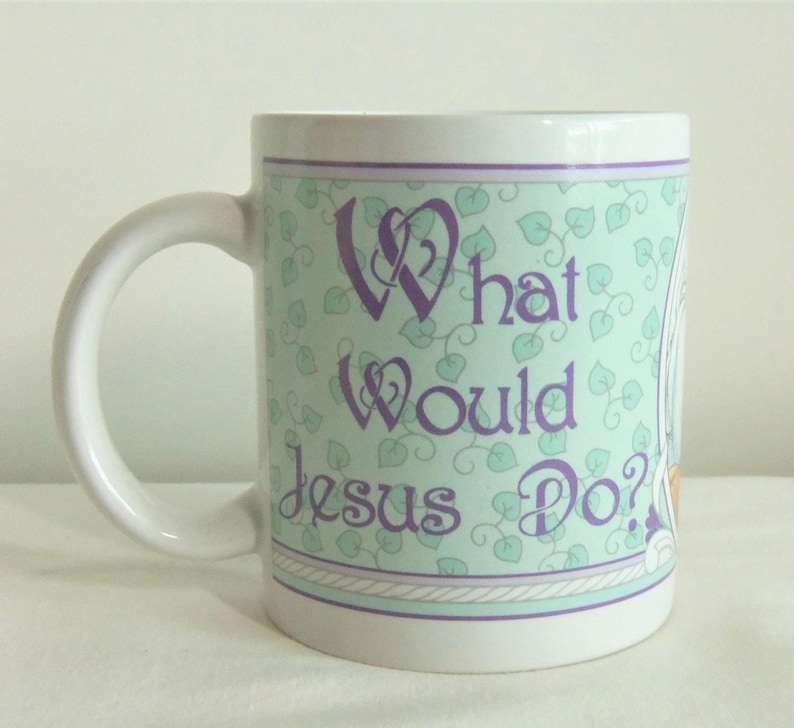 May include: A white ceramic mug featuring a light green background with a repeating pattern of small leaves. The text "What Would Jesus Do?" is printed in purple script lettering on the front, framed by thin purple and white border lines.
