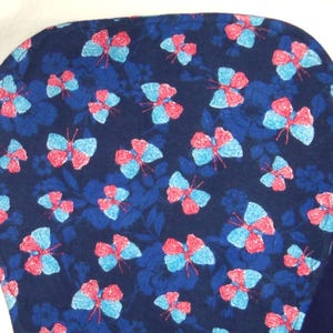 May include: A dark blue fabric with a repeating pattern of pink and blue butterflies. The fabric has a soft, fuzzy texture.