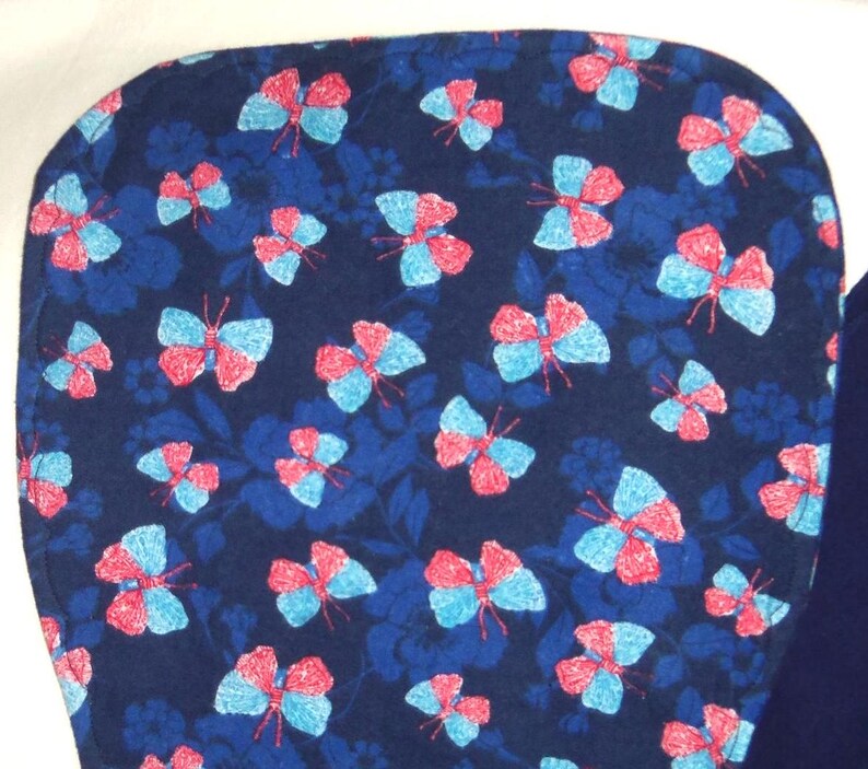 May include: A dark blue fabric with a repeating pattern of pink and blue butterflies. The fabric has a soft, fuzzy texture.