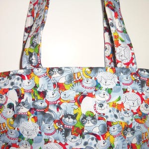 May include: A tote bag featuring a repeating pattern of cartoon cats in shades of gray, white, and black. The cats have expressive faces and wear red collars. The background includes vibrant splashes of yellow, green, and red colors throughout.