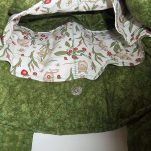 May include: A quilted green tote bag with a white interior lining featuring a repeating pattern of small brown mice, red strawberries, and white flowers. The bag includes a silver-toned metal magnetic snap closure centered on the inner green fabric.