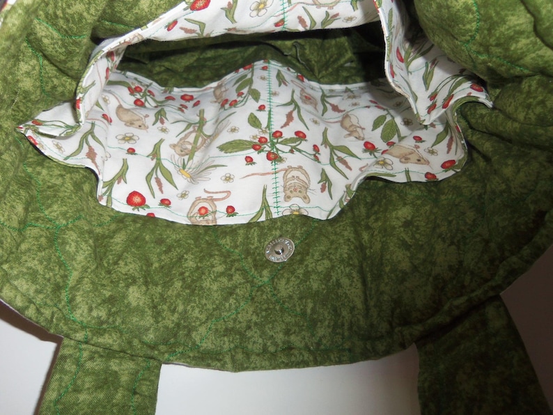 May include: A quilted green tote bag with a white interior lining featuring a repeating pattern of small brown mice, red strawberries, and white flowers. The bag includes a silver-toned metal magnetic snap closure centered on the inner green fabric.