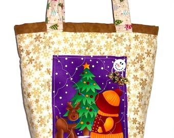 Könnte beinhalten: Eine gesteppte Tragetasche aus cremefarbenem Stoff mit goldenen Schneeflockenmustern, braunem Rand und Henkeln mit buntem Tannenbaumdruck. Ein zentrales violettes Feld zeigt ein Rentier, einen Weihnachtsbaum und eine Figur im roten Mantel, verziert mit einem Schneemann-Knopf und goldenen Glöckchen.