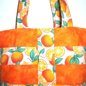 May include: A handmade tote bag with a vibrant orange and white citrus fruit pattern. The bag features a patchwork design with solid orange panels and handles, and a repeating pattern of oranges and green leaves. The bag is designed for carrying items.