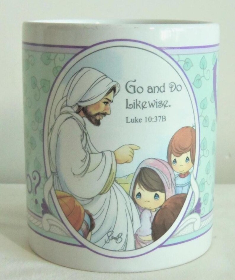 May include: A white ceramic mug featuring a central oval illustration of a bearded figure in a white robe pointing toward two children. The text "Go and Do Likewise. Luke 10:37B" is printed in black. The background has a light green ivy pattern.