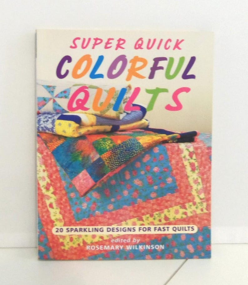 May include: A softcover book titled Super Quick Colorful Quilts edited by Rosemary Wilkinson. The cover features a stack of vibrant, multi-colored patchwork quilts with floral and geometric patterns. The text 20 Sparkling Designs for Fast Quilts is printed at the bottom.