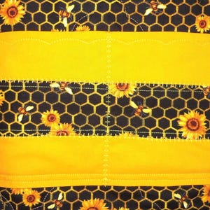 May include: A quilted fabric item featuring a black background with a yellow honeycomb pattern, sunflowers, and bees. The design includes horizontal solid yellow bands with scalloped edges and decorative stitching across the surface.